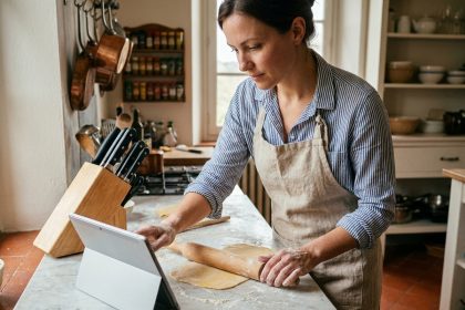 Femme suivant un cours de cuisine en ligne sur tablette tout en préparant des pâtes fraîches dans sa cuisine